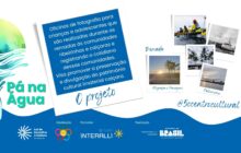 Material gráfico promocional do projeto Pá na Água. O plano de fundo é branco com uma grande faixa azul ondulada na base. À esquerda, o logo do projeto com as letras Pá na Água ao lado de um remo e uma pena abstrata nas cores verde e amarelo. No centro, um bloco de texto emoldurado como uma foto polaroid branca. O título é "O projeto". O texto descreve: "Oficinas de fotografia para crianças e adolescentes que são realizadas durante as remadas às comunidades ribeirinhas e caiçaras e registrando o cotidiano dessas comunidades. Visa promover a preservação e divulgação do patrimônio cultural imaterial caiçara." À direita, 4 pequenas fotos tipo polaroid flutuam no espaço branco. De cima para baixo e da esquerda para a direita, elas mostram: 1. Pessoas remando no mar, legendada "Remada". 2. Coqueiros sob sol forte na praia, legendada "Fotografia e Paisagens". 3. Um barco ancorado na margem e construções, legendada "Patrimônio". 4. Uma embarcação atracada em preto e branco. A hashtag "5ccentroCultural" está abaixo das fotos. Na faixa azul inferior, os logos da Lei de Incentivo à Cultura, Grupo Interalli e Governo do Brasil.